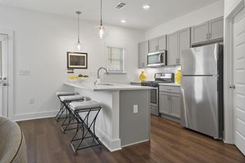 A kitchen with a white quartz countertop with pendant lighting and stainless-steel appliances.